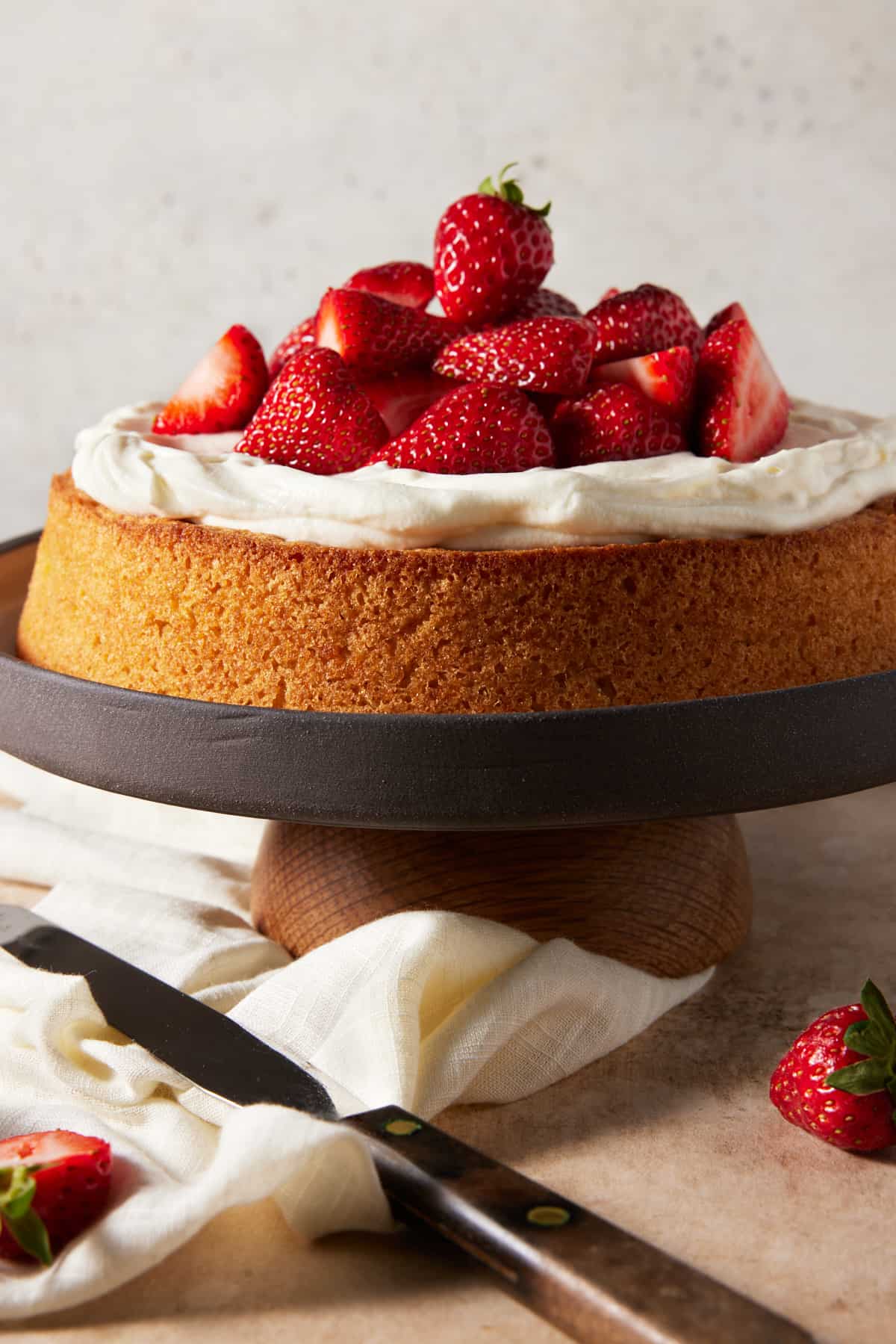 Almond cake on cake stand topped with whipped cream and strawberries. 