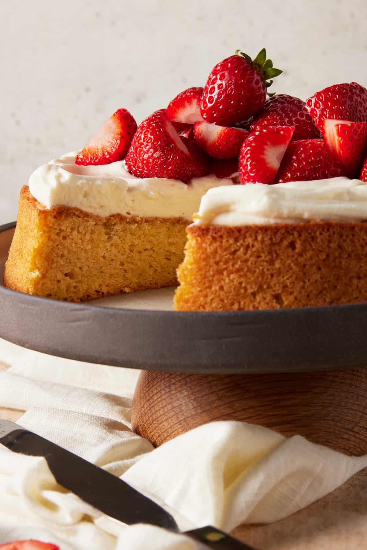 Almond Flour Cake on cake stand with piece removed. Topped with cream and strawberries. 