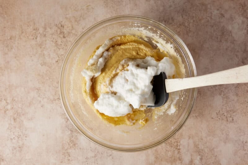 Beaten egg whites folded into almond flour cake batter in a glass bowl. 