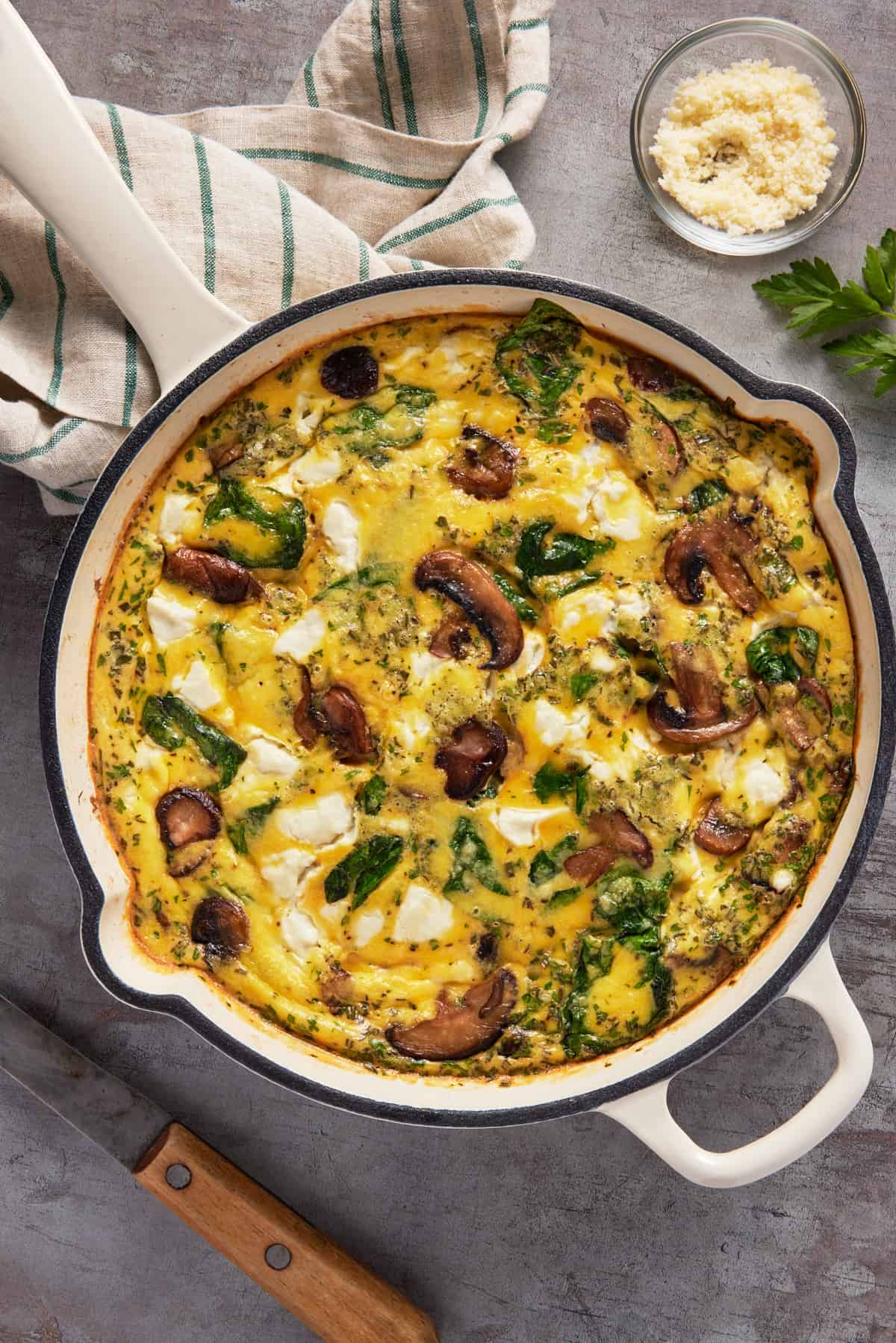 Mushroom and goat cheese frittata in a white enameled cast iron skillet with a striped kitchen towel. 