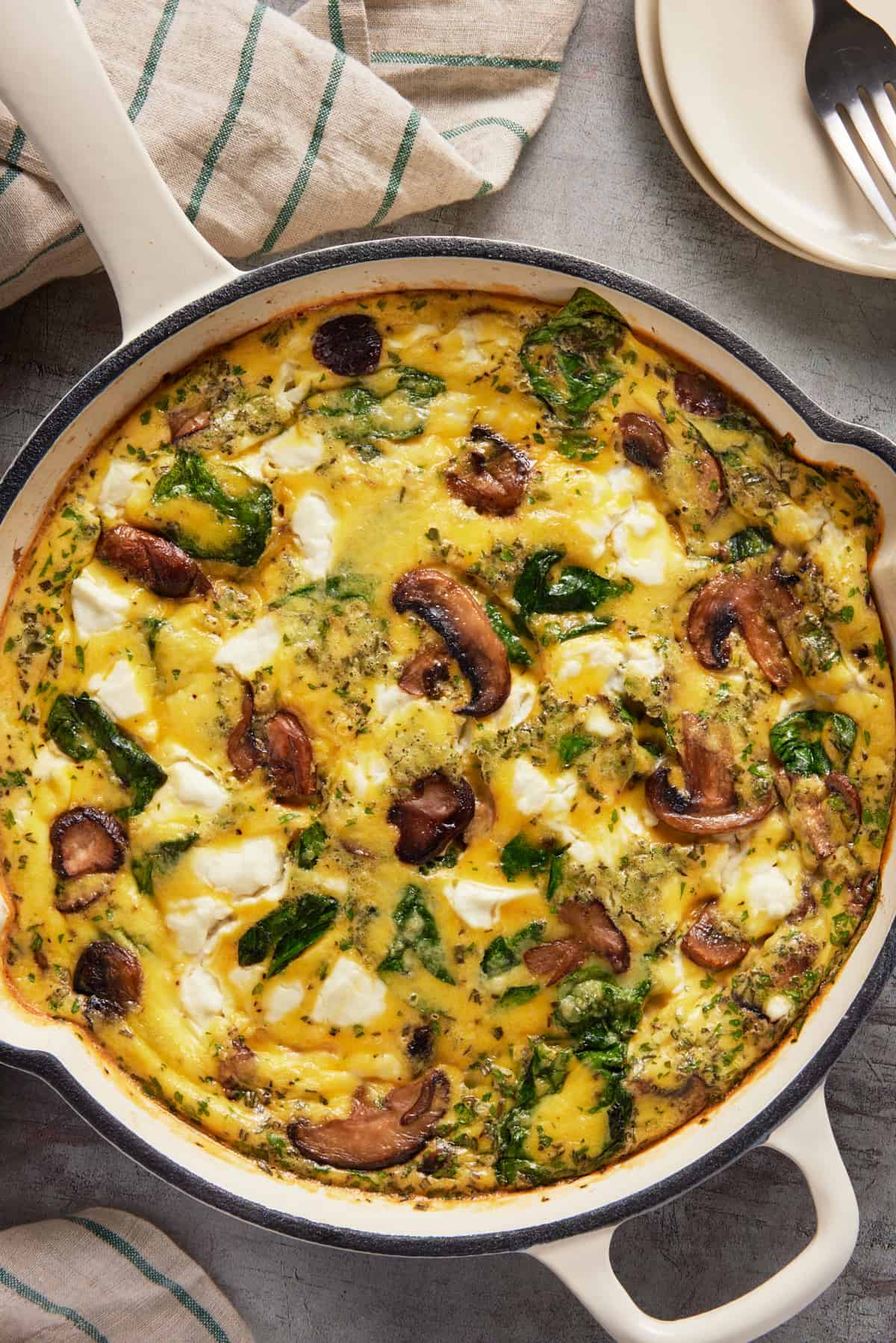 Spinach, mushroom and goat cheese frittata in a white cast iron enameled skillet.