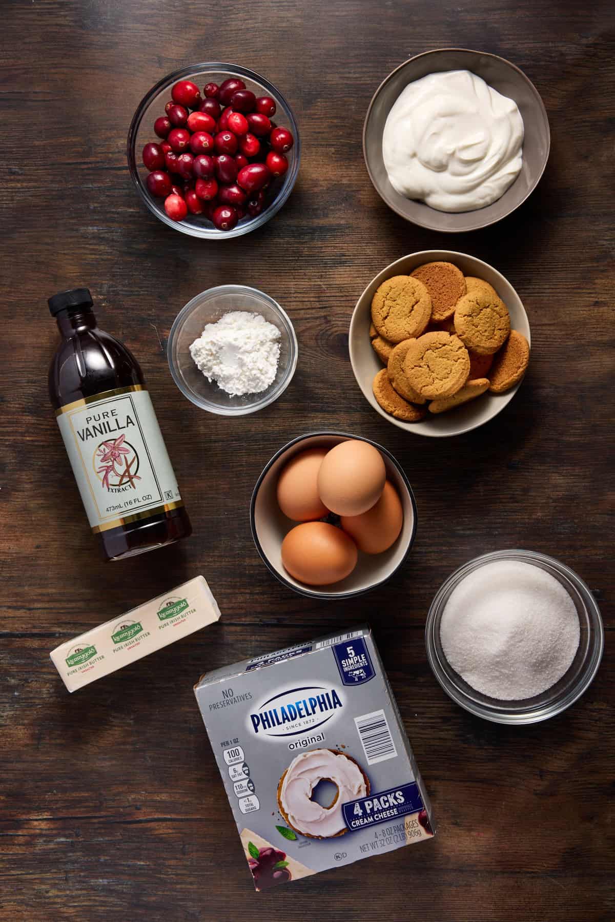 Bowls of ingredients for cranberry cheesecake including cranberries, gingersnaps, eggs and cream cheese. 