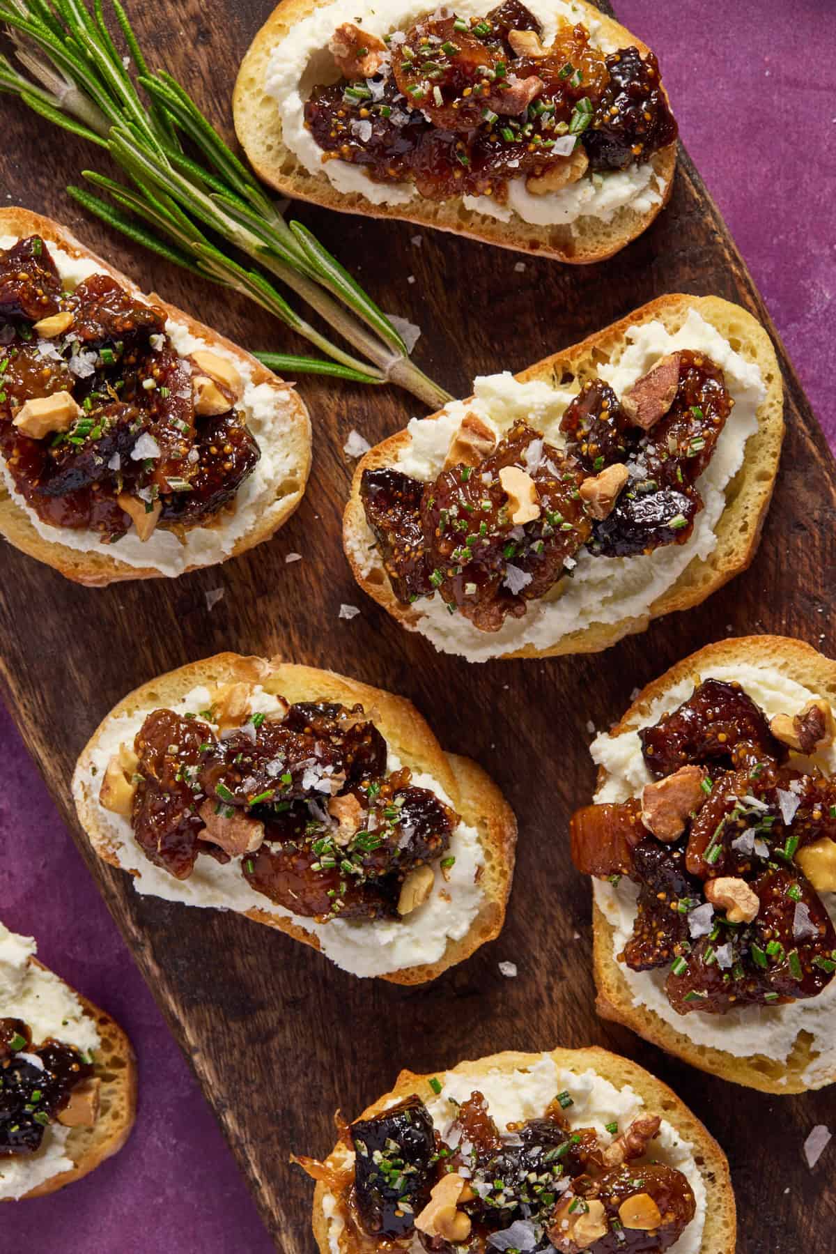 Close up of fig and goat cheese crostini sprinkled with chopped rosemary, walnuts and sea salt. 