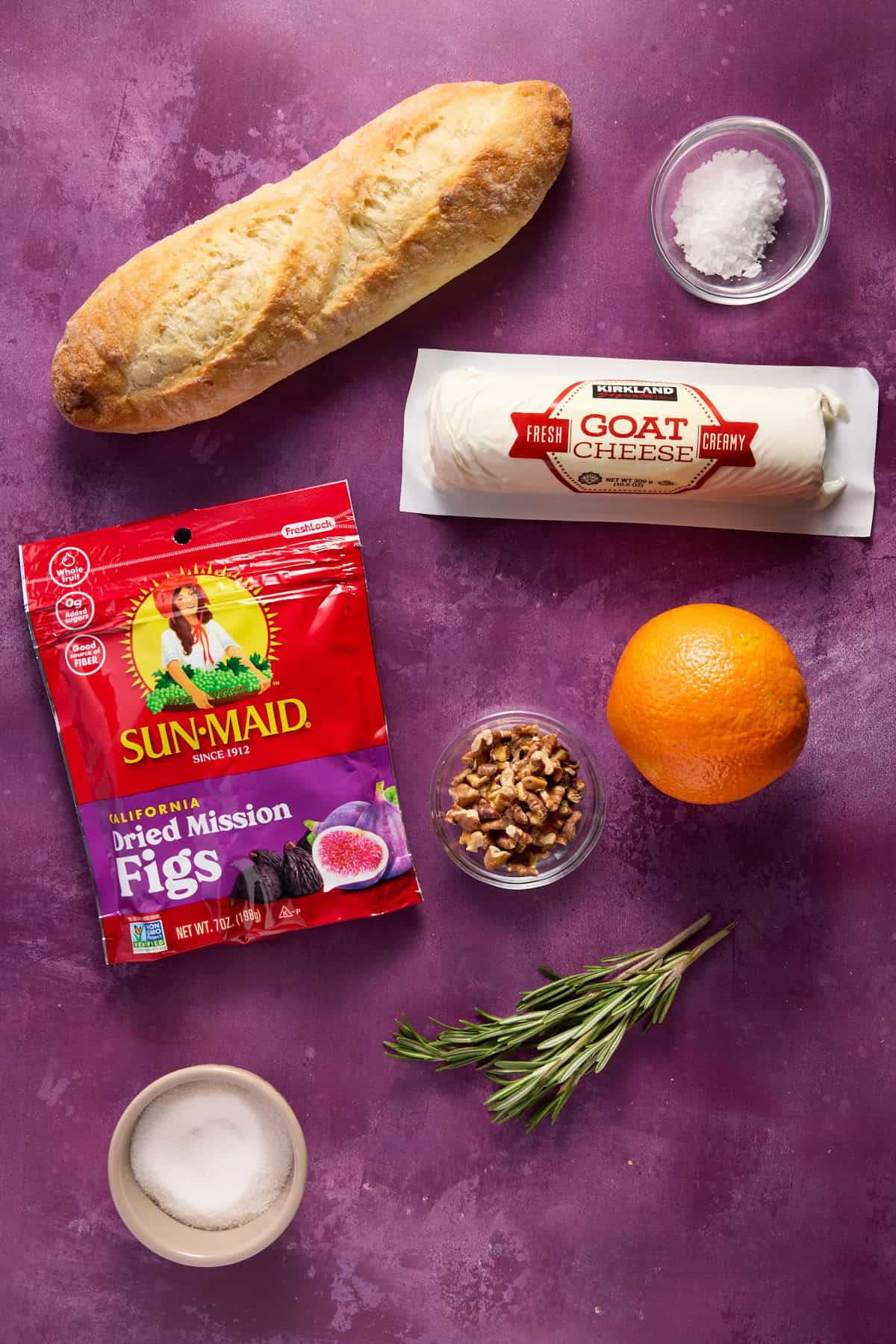 Ingredients needed to make fig and goat cheese crostini, including a baguette, figs, goat cheese and rosemary. 