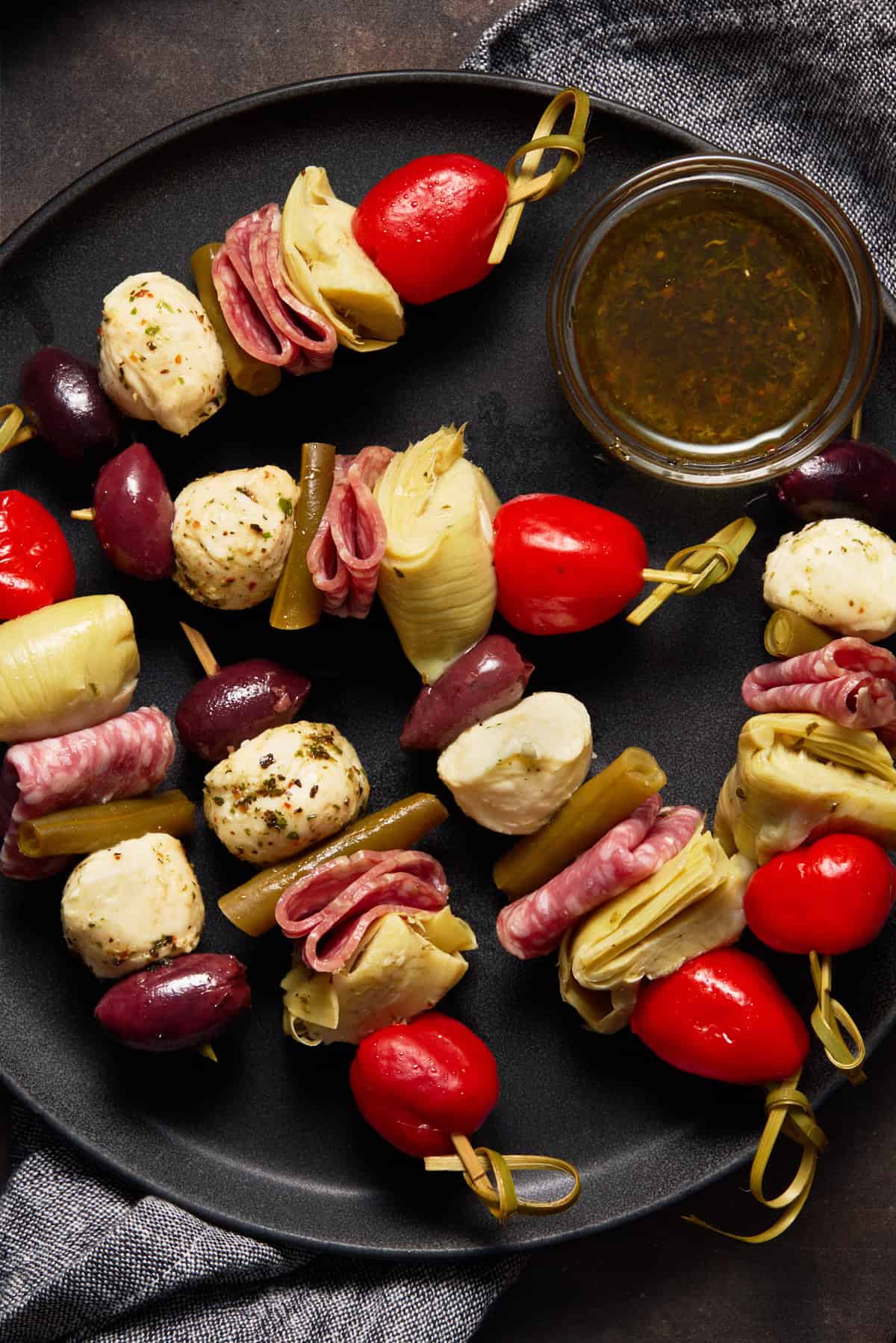 Several skewers on gray plate with oil dipping sauce in bowl.