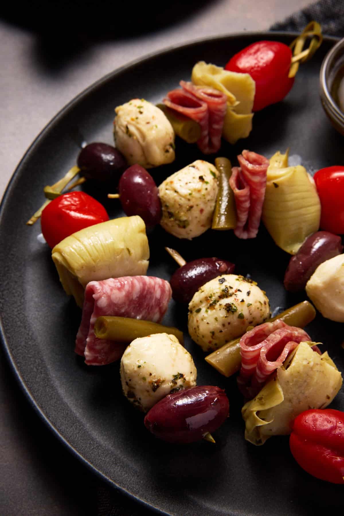 Italian skewers on a plate with olives, marinated cheese and cherry peppers.