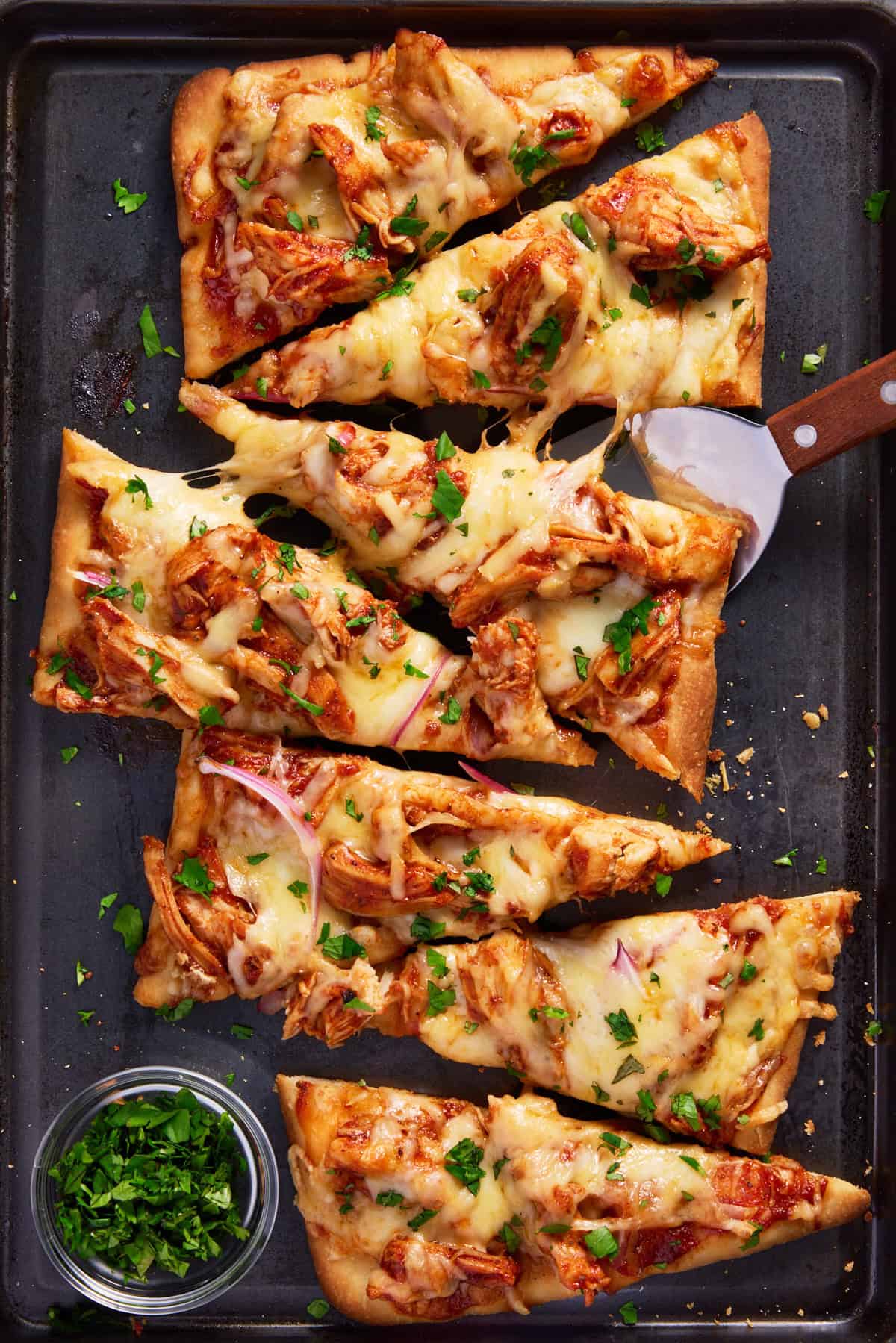 Slices of BBQ Chicken Flatbread sprinkled with cilantro on a black sheet pan. 