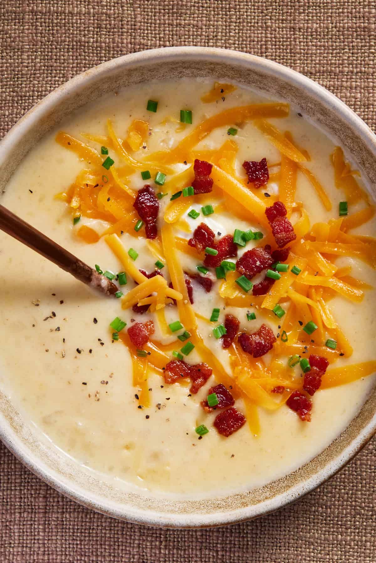 Bowl of Baked Potato Soup topped with bacon bits, chopped chives and cheddar cheese. 