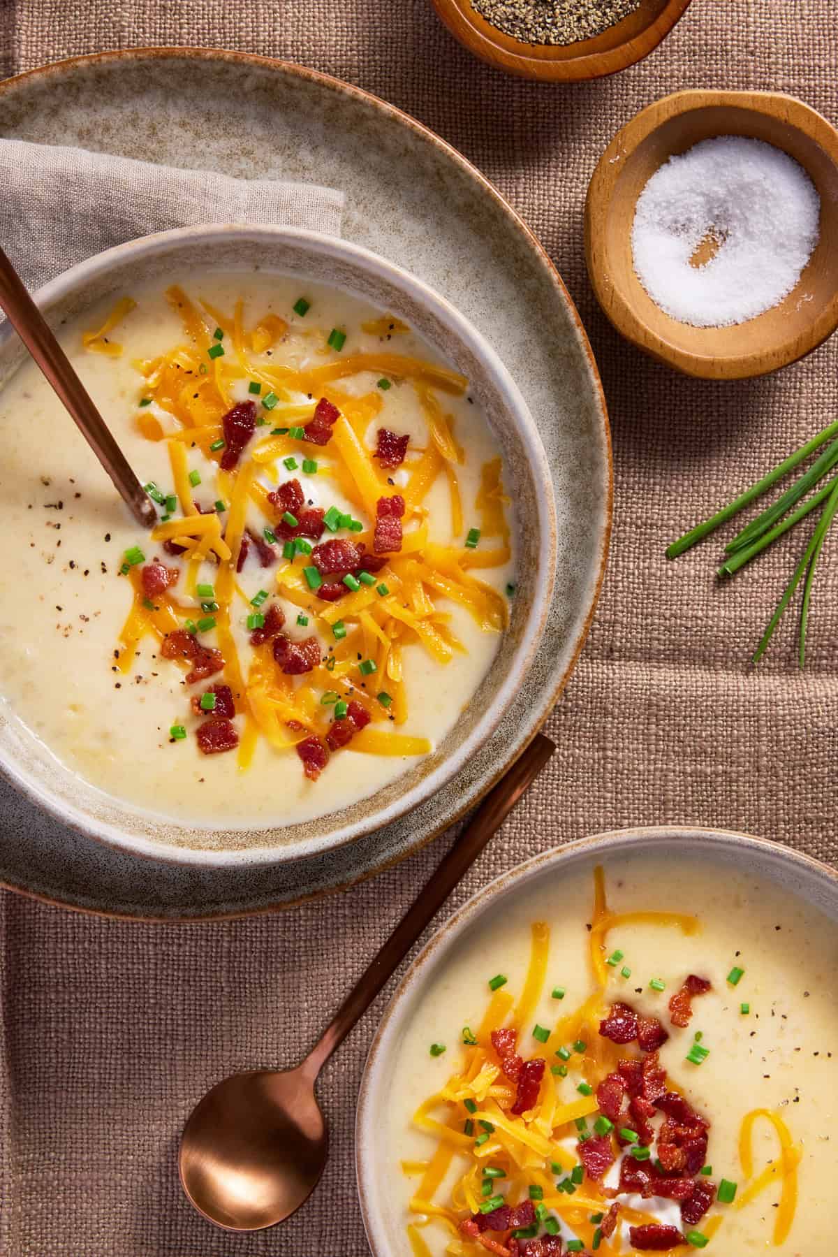 Two bowls of baked potato soup topped with cheese, bacon and chives. 