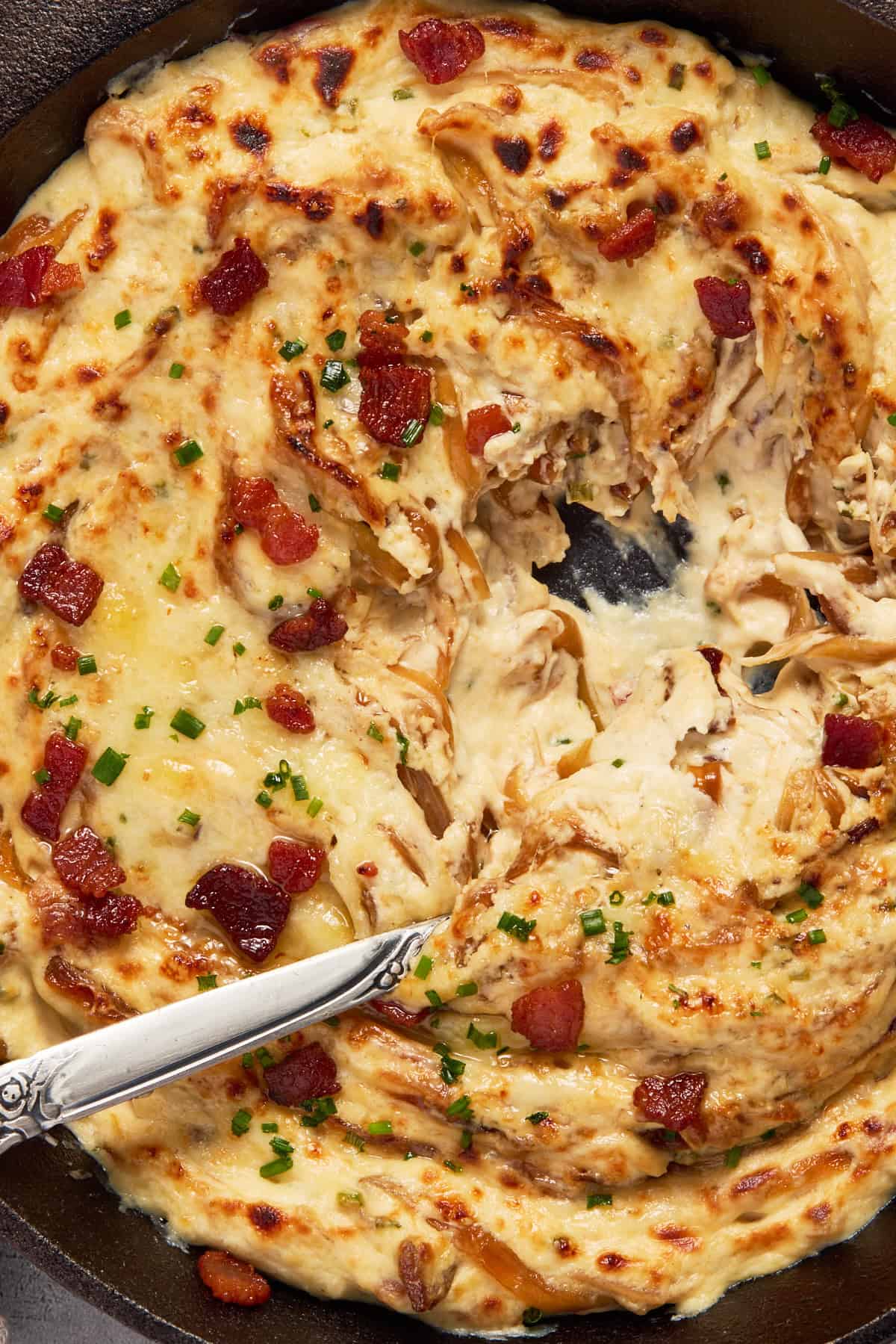 Cheesy caramelized onion dip with a spoon and fresh chives.