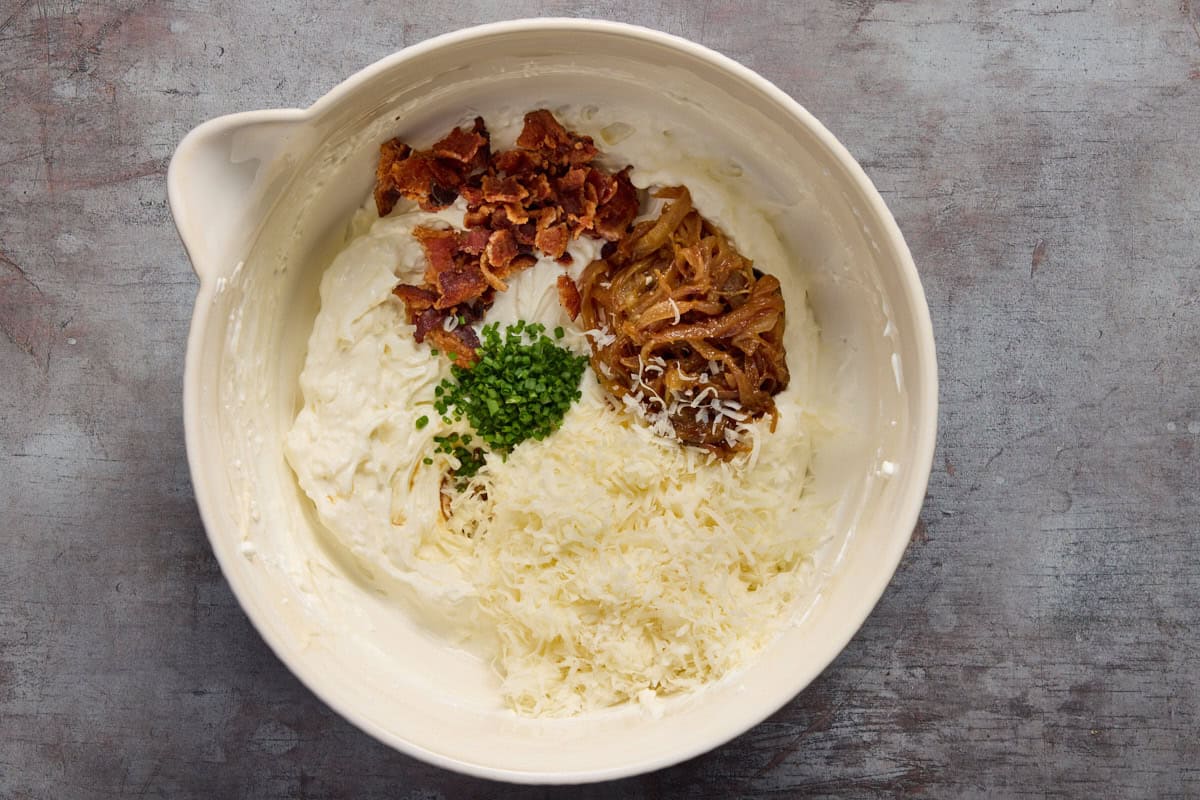 Cream cheese, sour cream in bowl with bacon, onions, cheese.