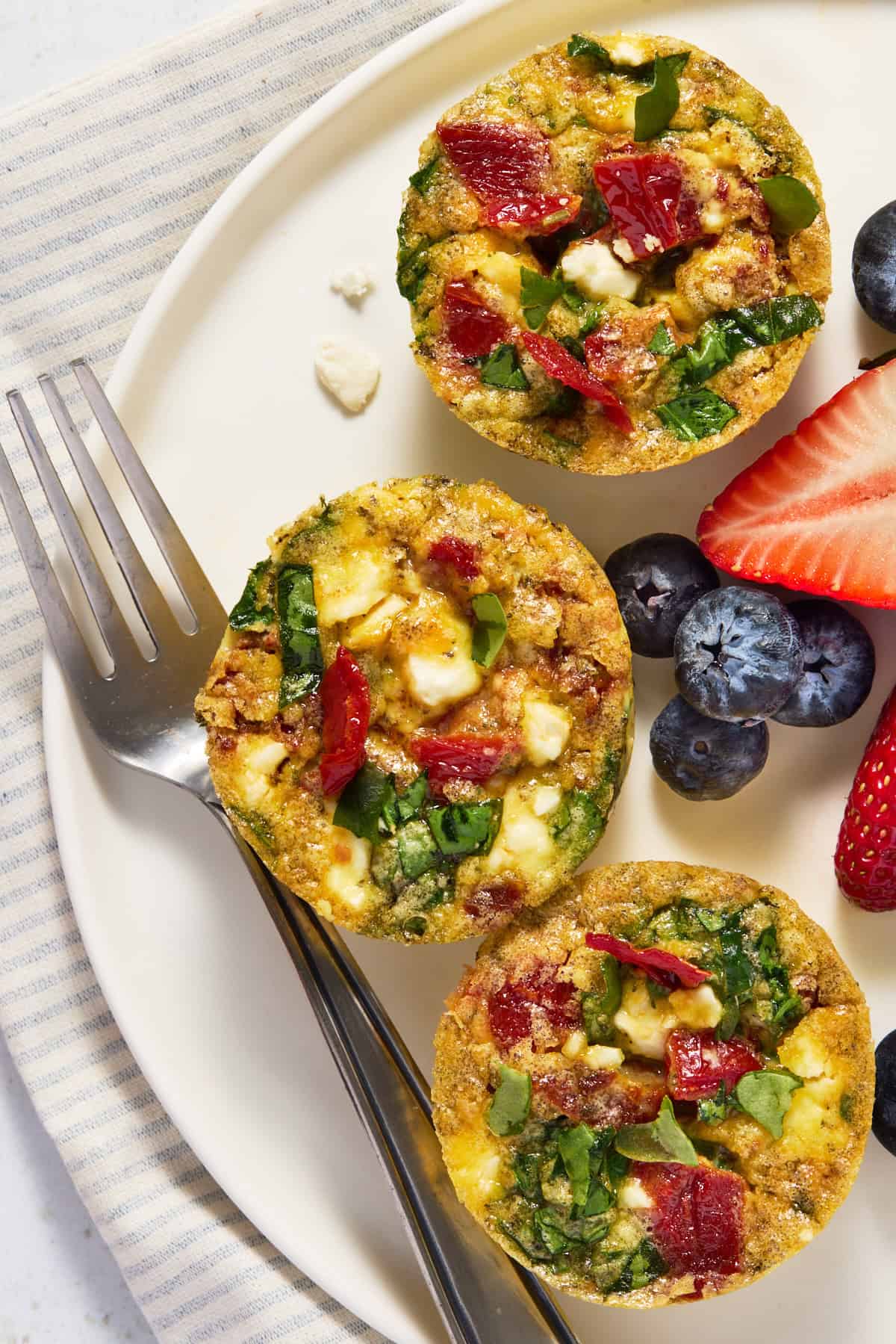 Three breakfast egg muffins on a white plate with berries.
