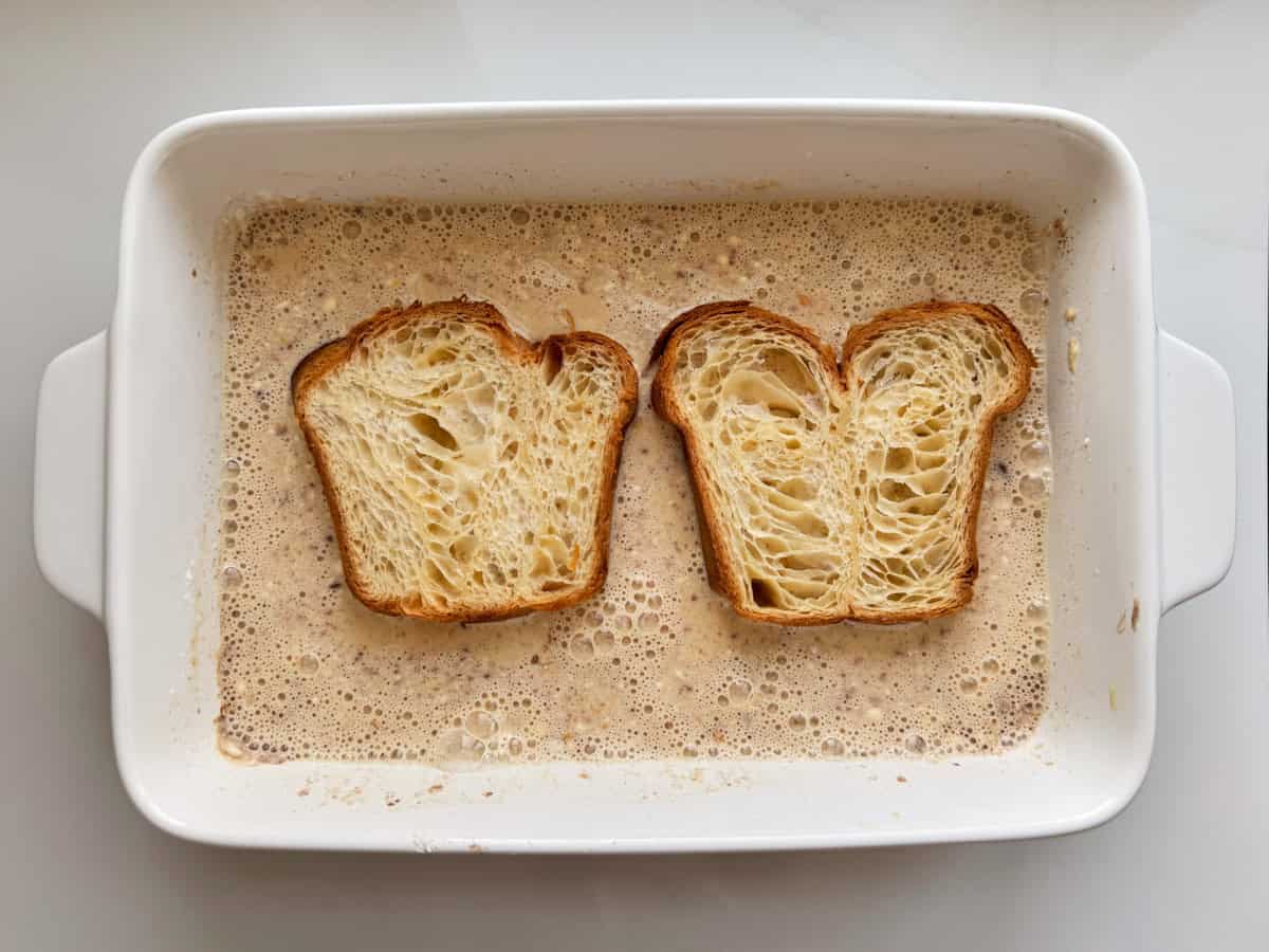 Two pieces of croissant bread in french toast batter. 