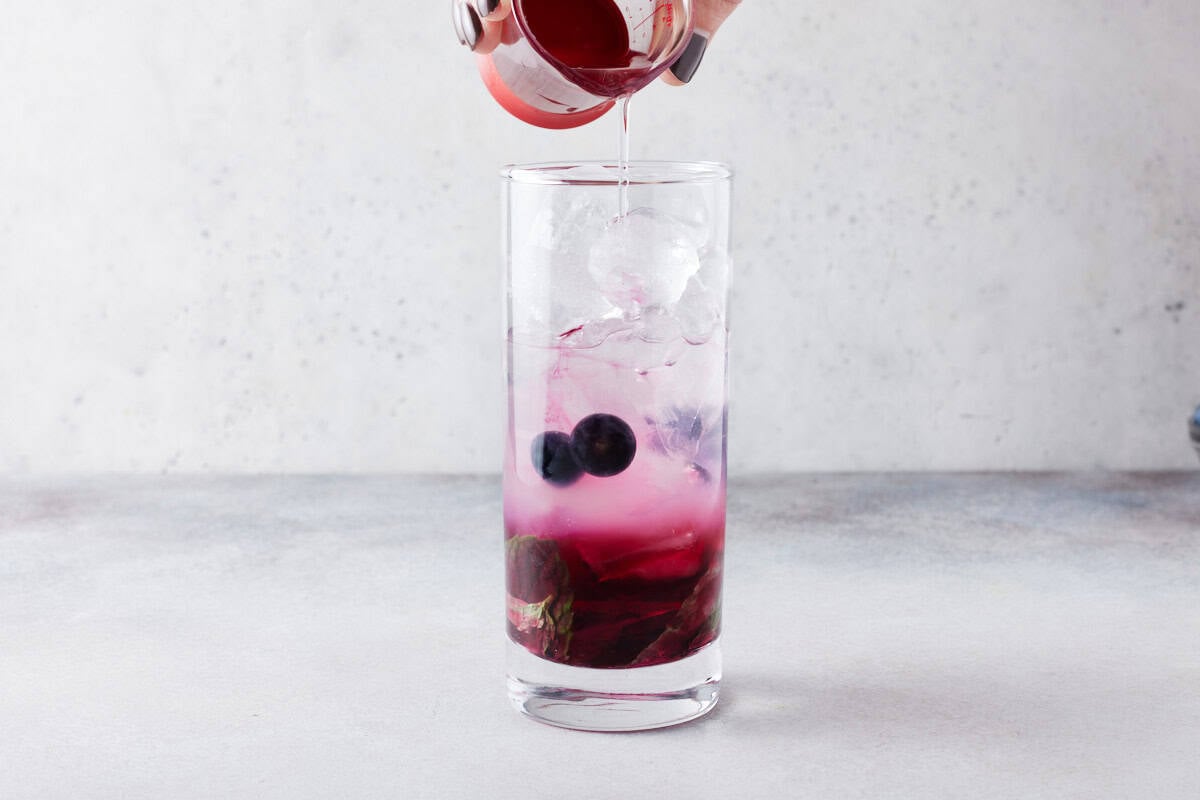 Tall glass filled with ice and rum being poured in.