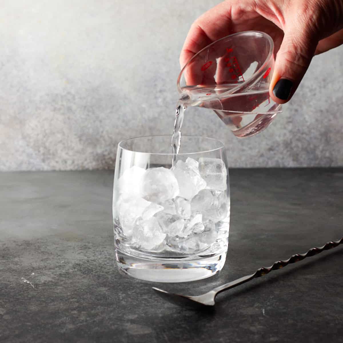 Low ball glass filled with ice with vodka being poured.