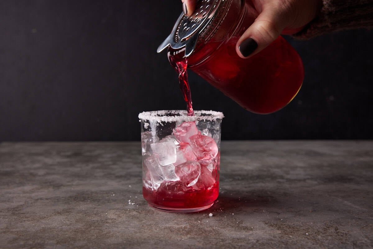 Cranberry margarita being strained into a salt rimmed glass filled with ice.