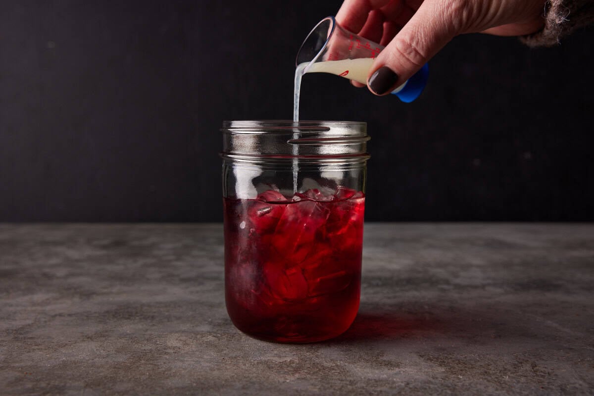 Lime juice being poured in a shaker full of cranberry juice.