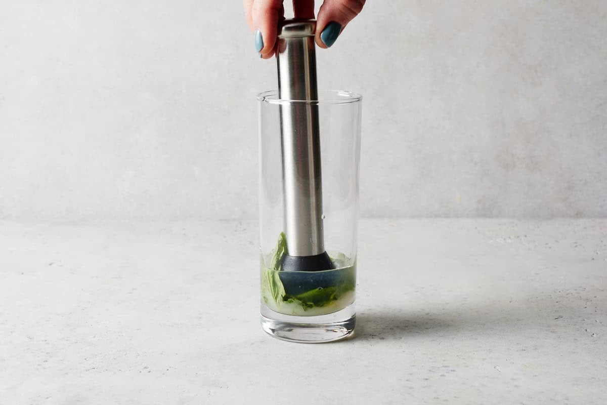Muddler in high ball glass with mint and lime juice.