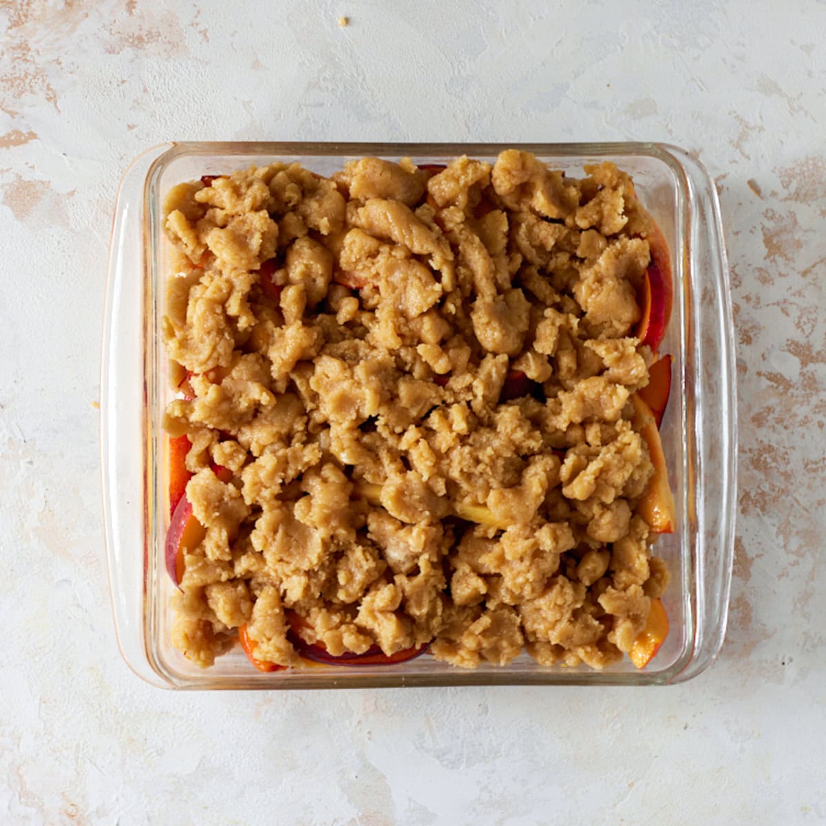 Sliced peaches with crumble topping on top ready to bake.