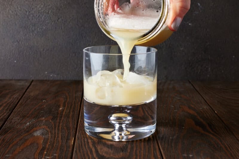 Shaken tequila sour being poured in ice filled glass.