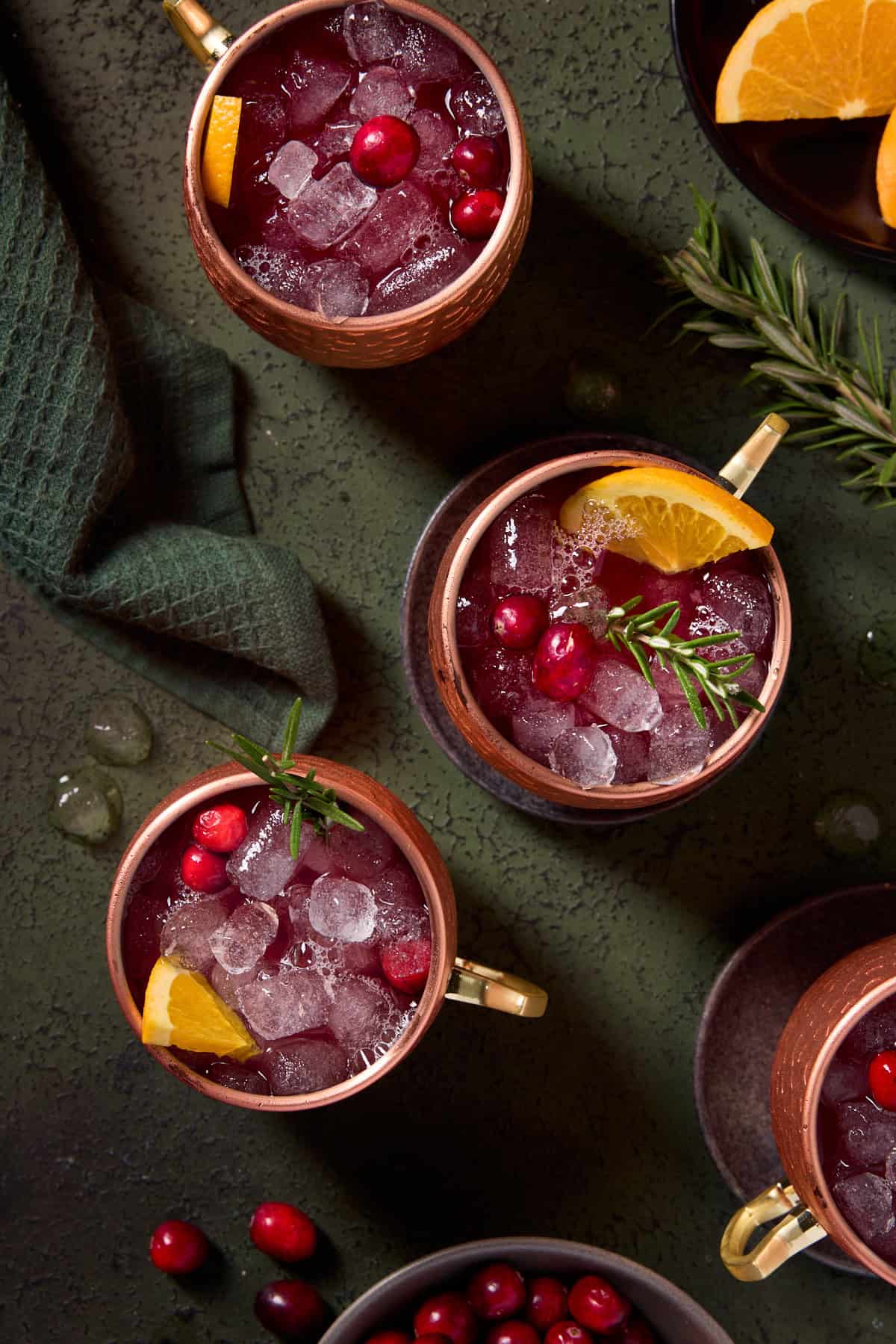 Top down image of 4 cranberry mules in copper mugs garnished with fresh rosemary, cranberries and orange slices.