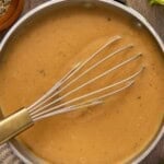 Gravy in a pan with a whisk and pepper on side.