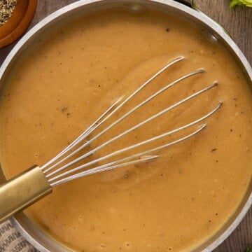 Gravy in a pan with a whisk and pepper on side.