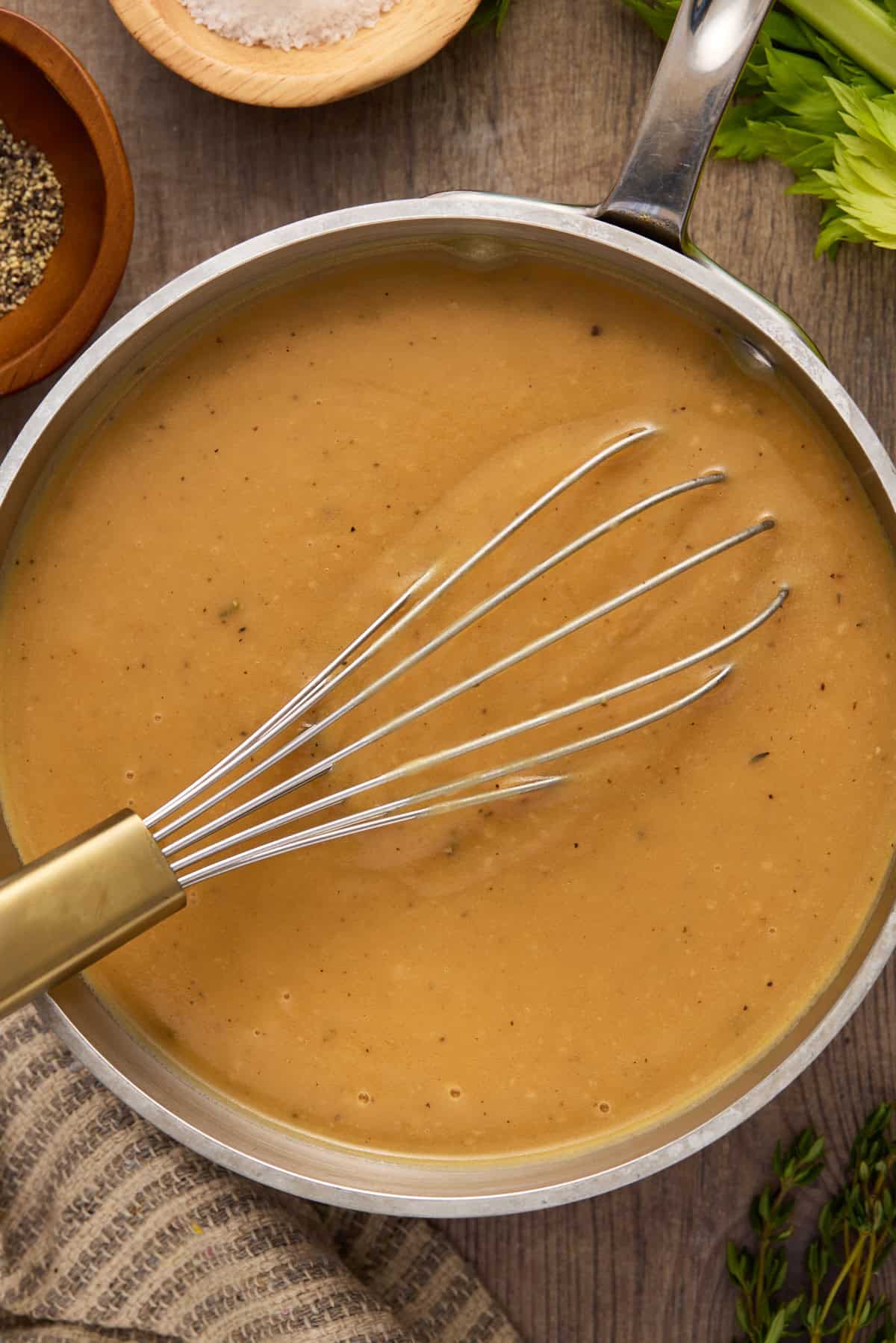Gravy in a pan with a whisk and salt and pepper on side.