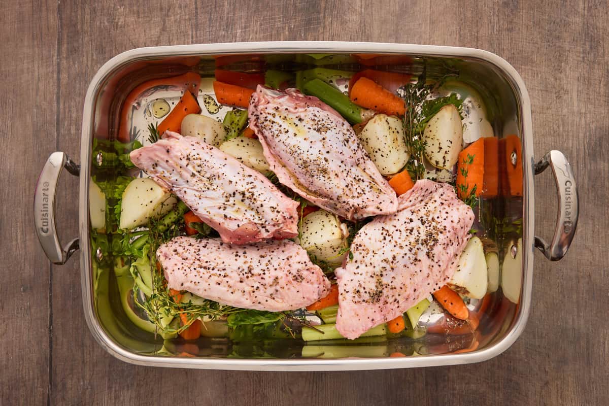 Turkey wings on top of chopped vegetables in a roasting pan.