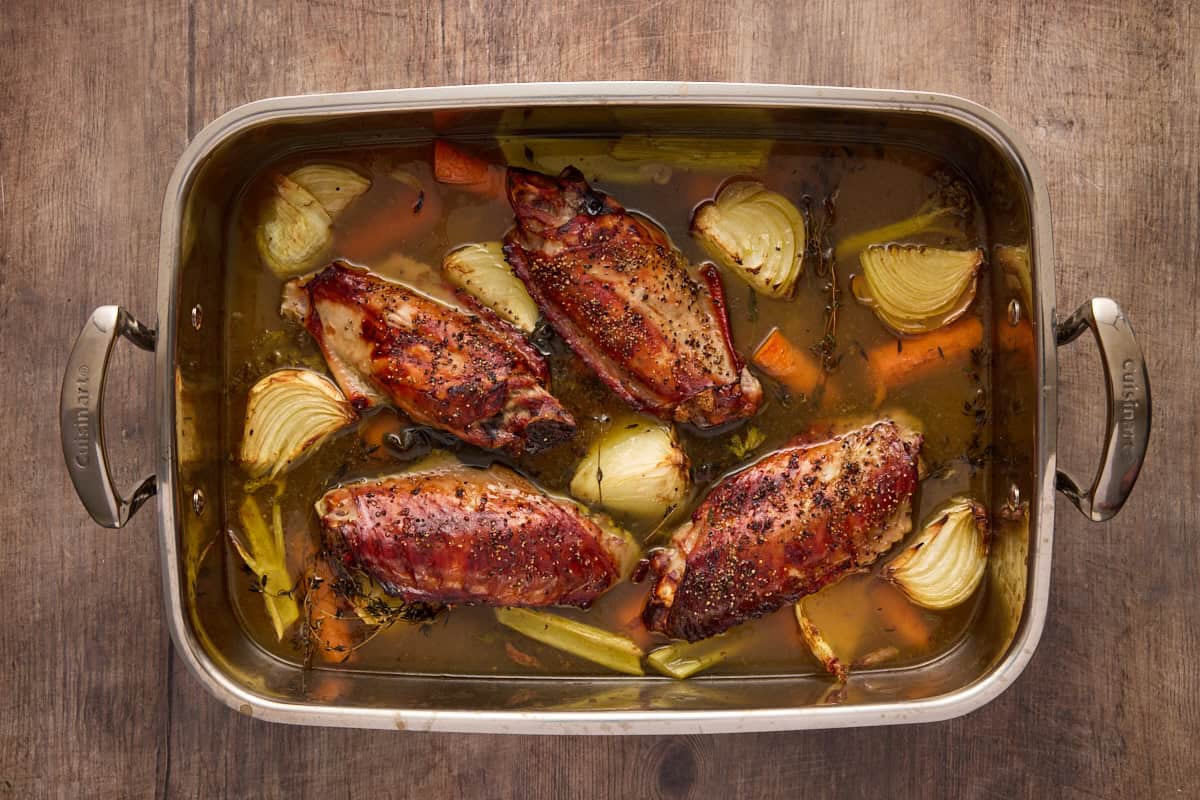 Roasted turkey wings with cooked vegetables and broth in a roasting pan.