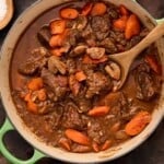 Green dutch oven filled with beef daube (french beef stew) with a wooden spoon.