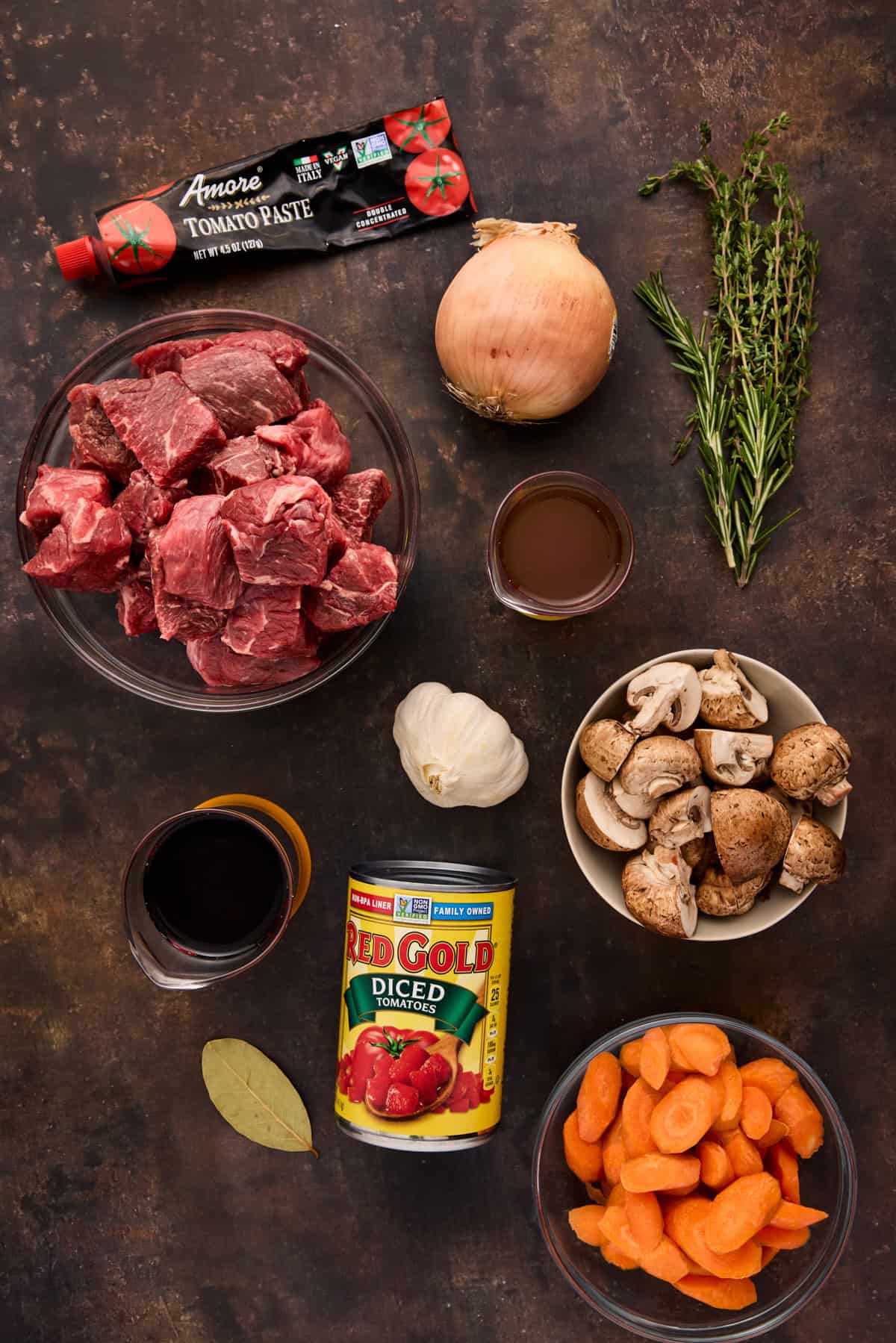 Ingredients for making beef daube (french beef stew) including beef, mushrooms, onions, garlic, tomatoes, carrots, herbs and red wine.