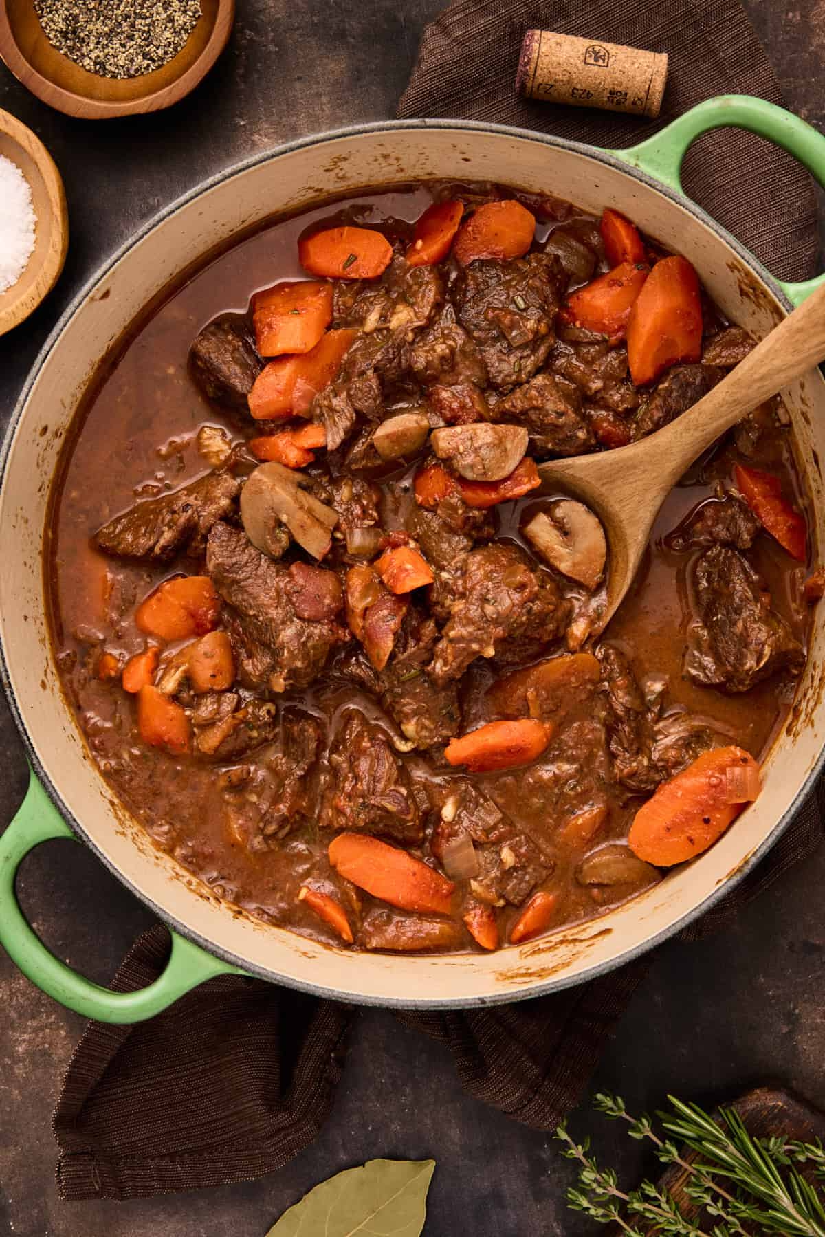 Green dutch oven filled with beef daube (french beef stew) with a wooden spoon.