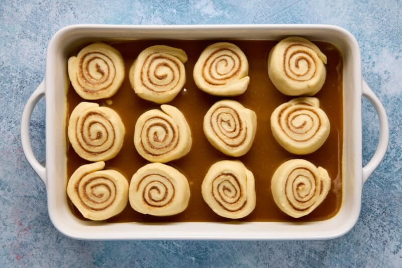 Raw caramel rolls in a white casserole dish with handles.