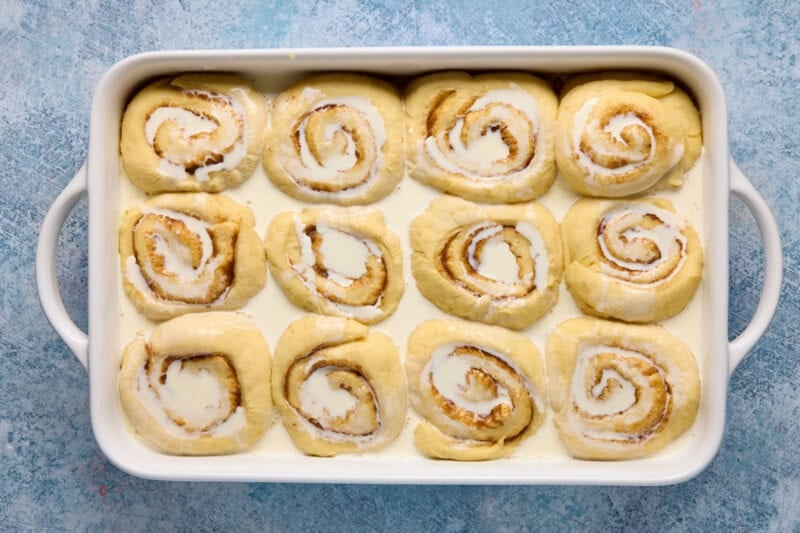Risen caramel rolls in a white casserole dish with cream poured on top.