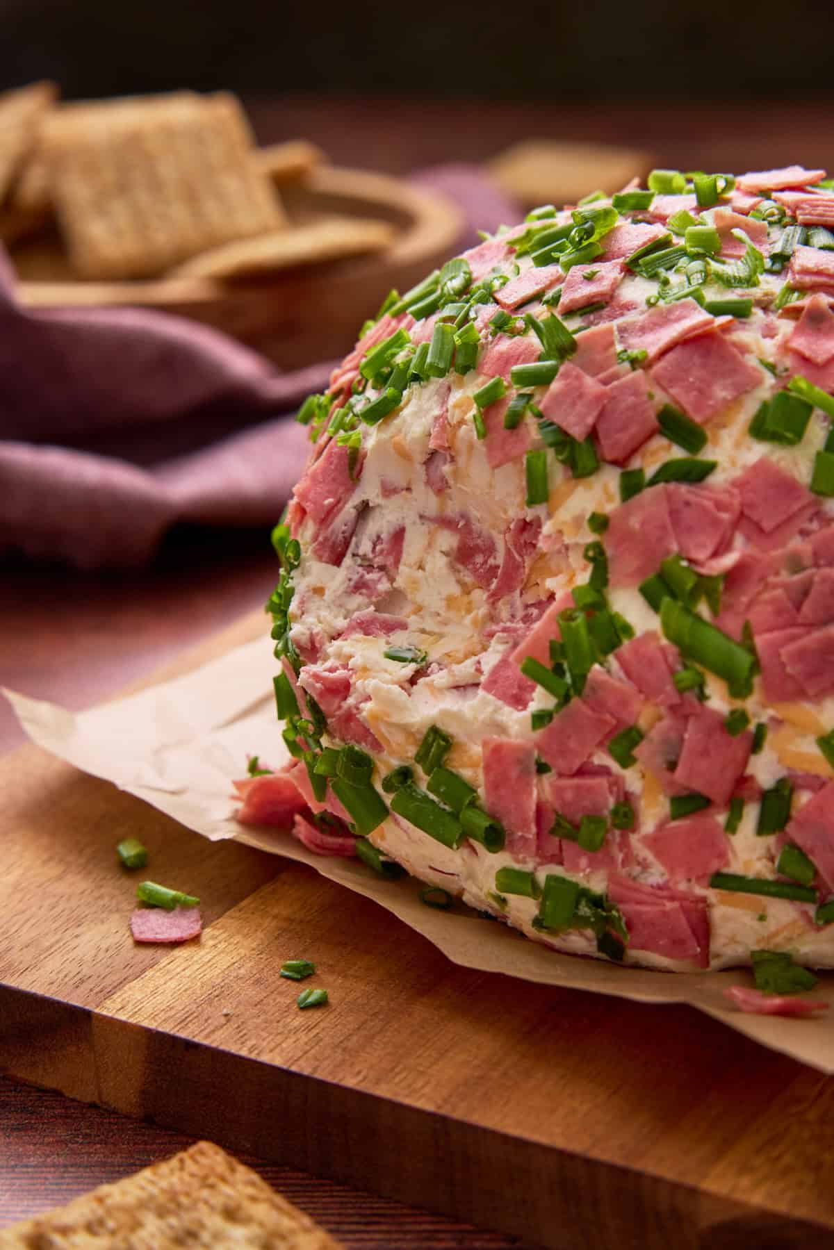Garnished chipped beef cheeseball on a board with crackers.