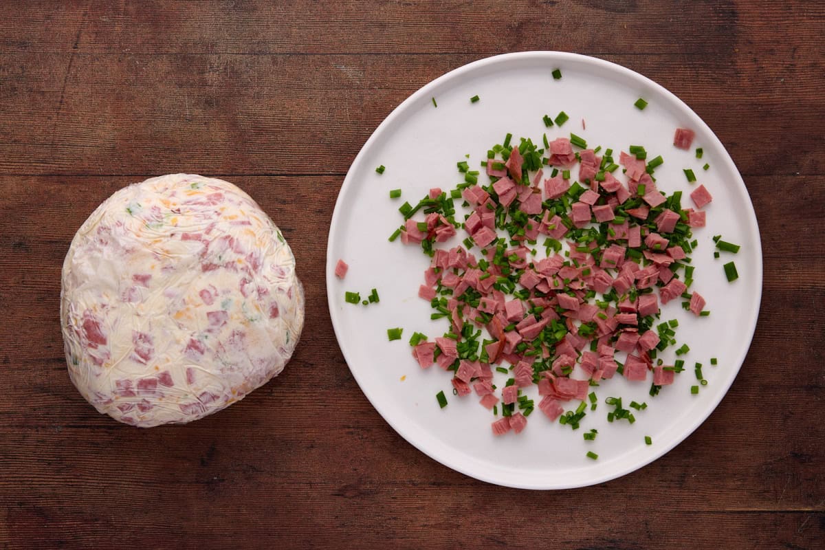 diced dried beef on white plate with chopped chives and a cheese ball wrapped in plastic.