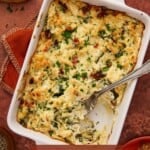 Crab artichoke dip in a white baking dish with crostini and a spoon.