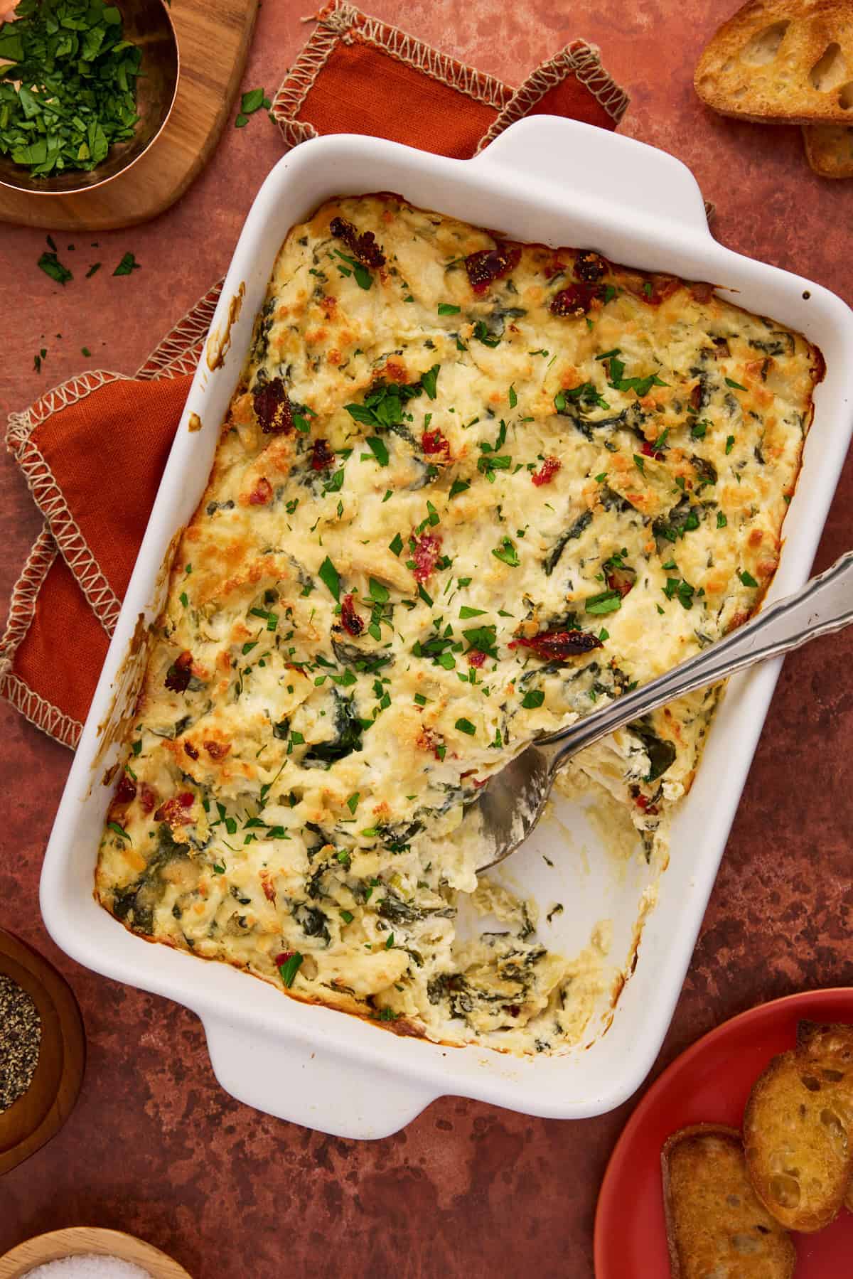 Crab spinach artichoke dip in white baking dish with a scoop out and a spoon in the pan.