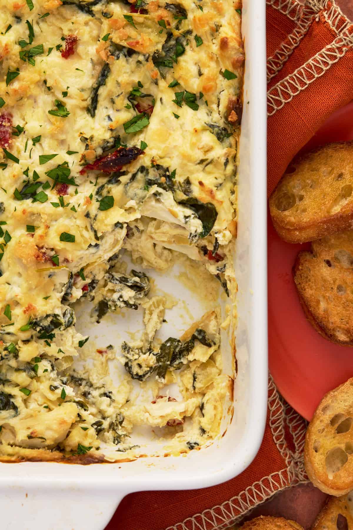 Crab Spinach artichoke dip in white pan with crostini.