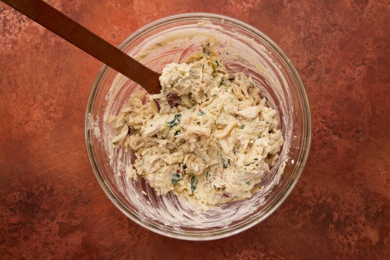 glass bowl with artichoke dip ingredients mixed in.