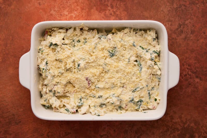 white baking dish ready to go in oven with artichoke dip and grated parmesan.