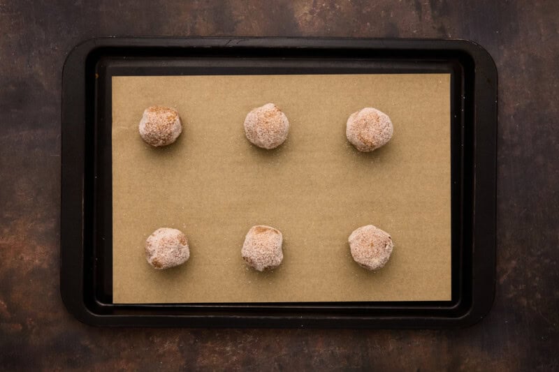 Molasses cookies dough rolled in sugar on baking sheet.