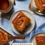 Four caramel rolls on small plates next to sheet pan of rolls and coffee cups.