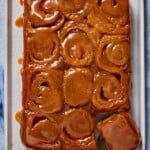 Sheet pan with 12 gooey caramel rolls and a wooden handle lifter.