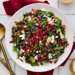 Holiday Salad with wild rice, pecans, goat cheese, apples and arugula on a white plate with a red napkin.