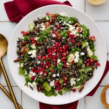 Holiday Salad with wild rice, pecans, goat cheese, apples and arugula on a white plate with a red napkin.