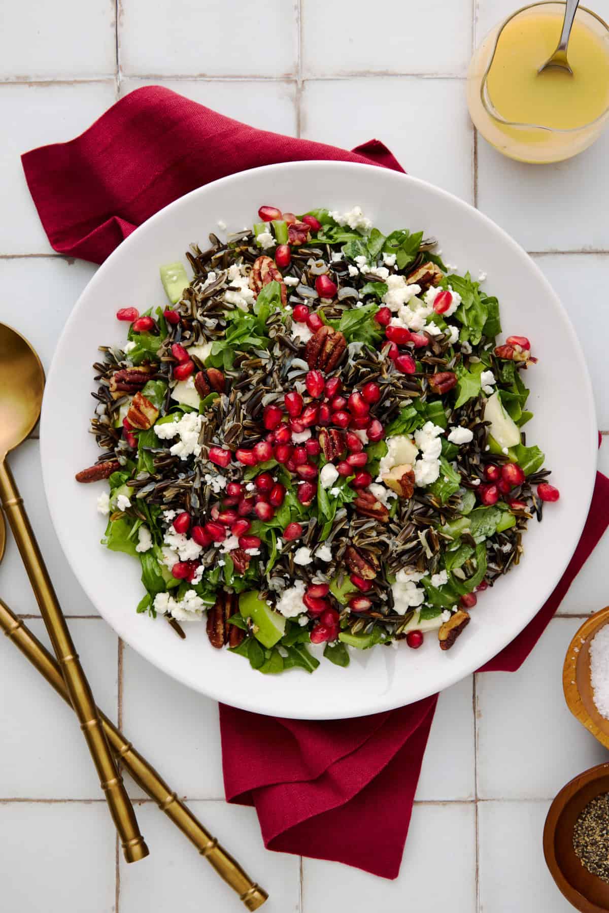 Top down shot of a holiday wild rice salad with arugula, pomegranate and goat cheese on a white plate with a red napkin.