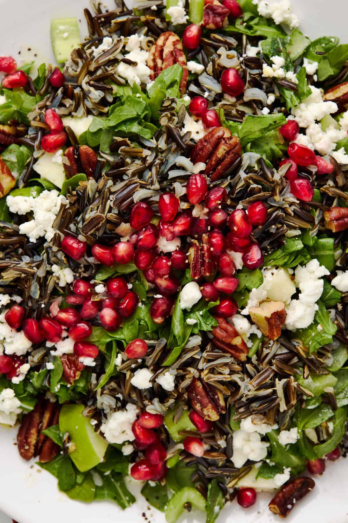 Close up of holiday salad with wild rice, pomegranate and arugula on a white plate.