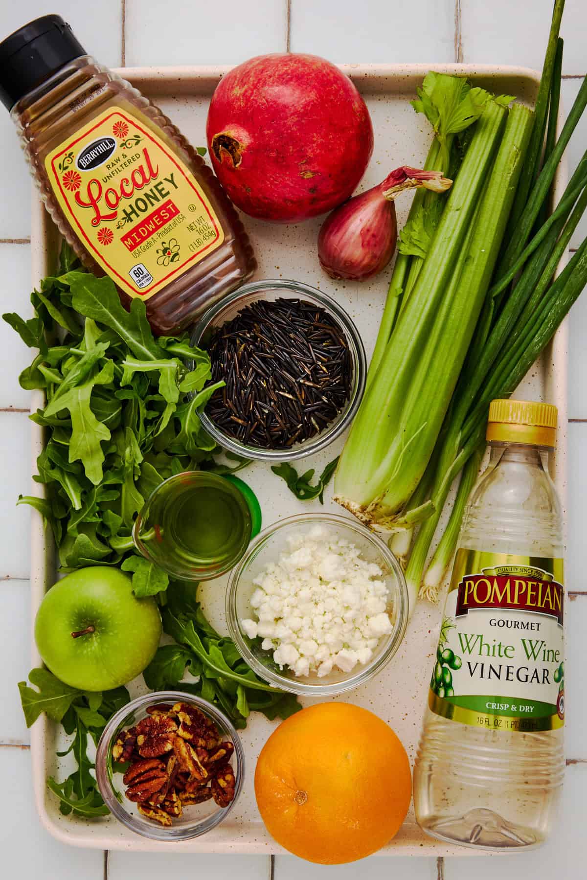 Ingredients for a holiday wild rice salad on a sheet pan including wild rice, pomegranate, shallot, arugula and goat cheese.